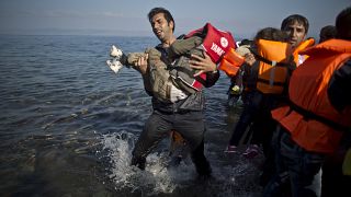 A man holds up a small child in a lifejacket after being brought ashore from a sinking ship in the Mediterranean