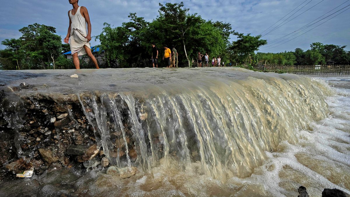 قرويون يخوضون في طريق دمرته مياه الفيضانات في قرية تشاماتا، غرب غواهاتي في الهند