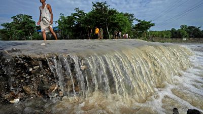 قرويون يخوضون في طريق دمرته مياه الفيضانات في قرية تشاماتا، غرب غواهاتي في الهند