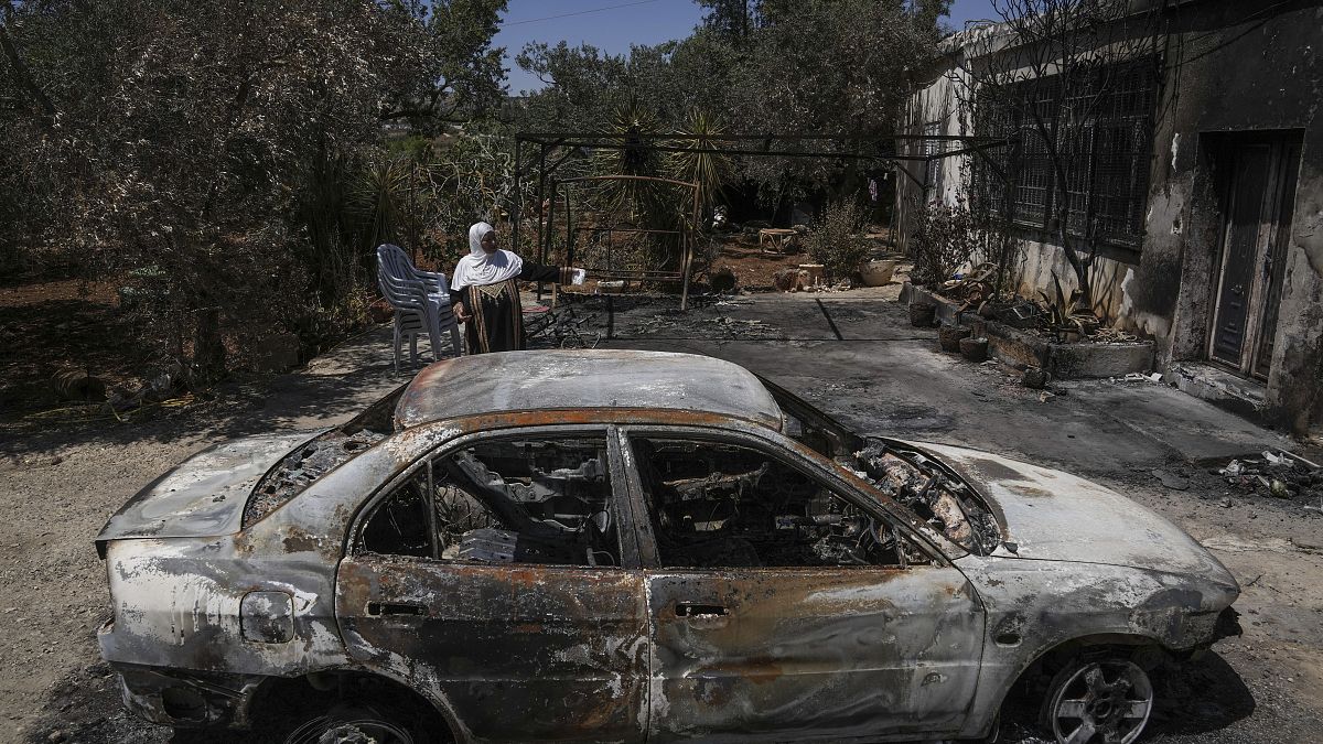 سيدة فلسطينية محجبة تقف بجوار سيارة تعرضت للحرق في ترمسعيا 