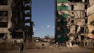 امرأة تقف بجوار مبنى سكني مدمر قبل عام في بورودينكا أوكرانيا يوم 2 مارس 2023.