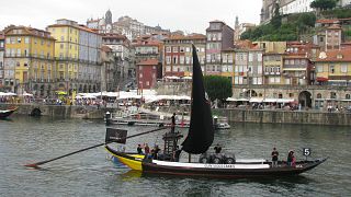 Perspetiva de um barco rabelo no Douro com a baixa do Porto em fundo