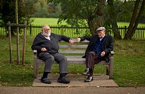 Two men sit on a bench on the periphery of the Hampstead Heath Heritage Festival, which is a celebration of old England on Hampstead Heath in London, Sunday, Oct. 7, 2012.