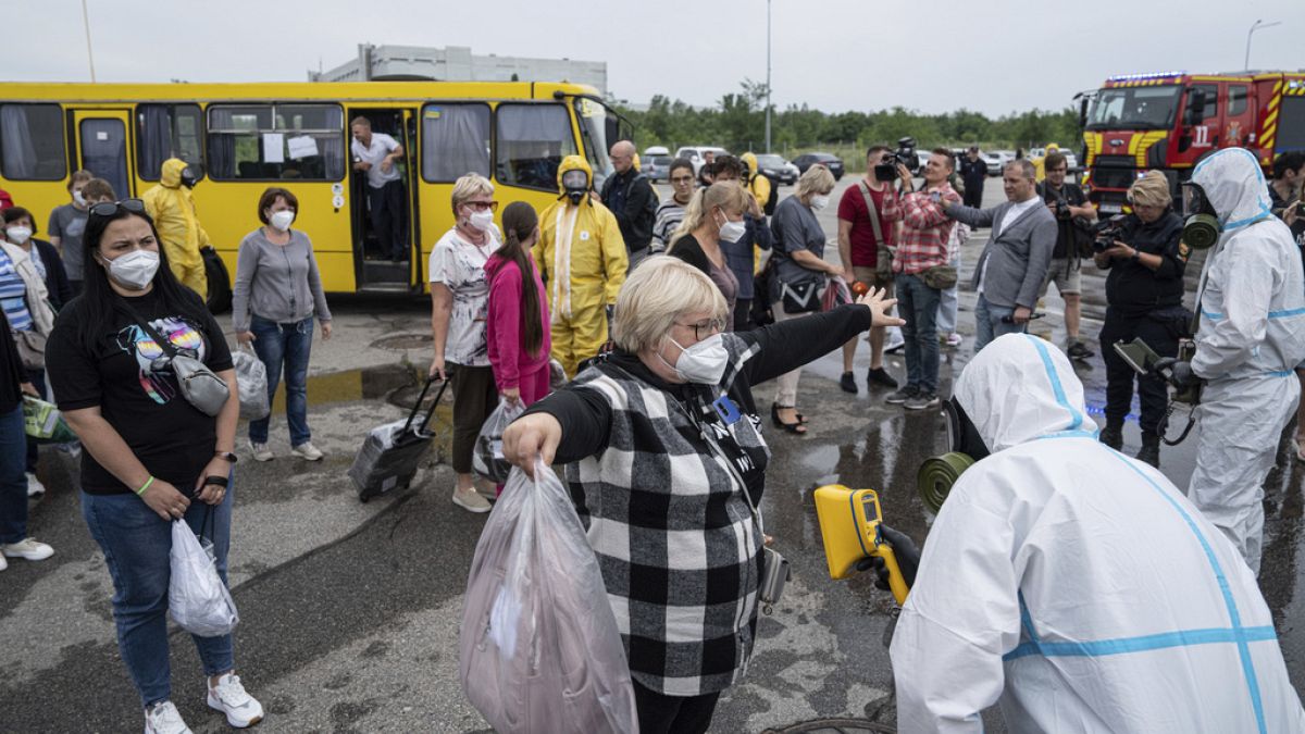 Trabajadores de emergencias ucranianos con trajes de protección radiológica comprueban el nivel de radiación de pasajeros en Zaporiyia, Ucrania, el jueves 29 de junio de 2023.