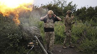 A Ukrainian servicemen of the 3rd separate assault brigade speaks on the radio while another serviceman is firing 82mm mortar towards Russian positions at the frontline