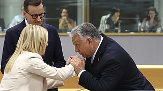 Orban bacia le mani di Giorgia Meloni, sotto lo sguardo di Morawiecki.(Bruxelles, 30.6.2023)