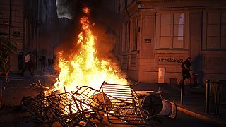 A man passes by a wall illuminated by a burning barricade on which is written 'Police kills' in the center of Lyon, central France, Friday, June 30, 2023. 