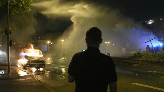 Los bomberos utilizan una manguera de agua en un coche quemado en Nanterre, a las afueras de París, Francia, sábado 1 de julio de 2023.
