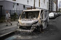 رجل يمر بجانب مركبة احترقت كليا جراء الاحتجاجات بحي كولومبس خارج العاصمة الفرسية باريس