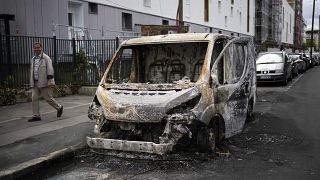 رجل يمر بجانب مركبة احترقت كليا جراء الاحتجاجات بحي كولومبس خارج العاصمة الفرسية باريس