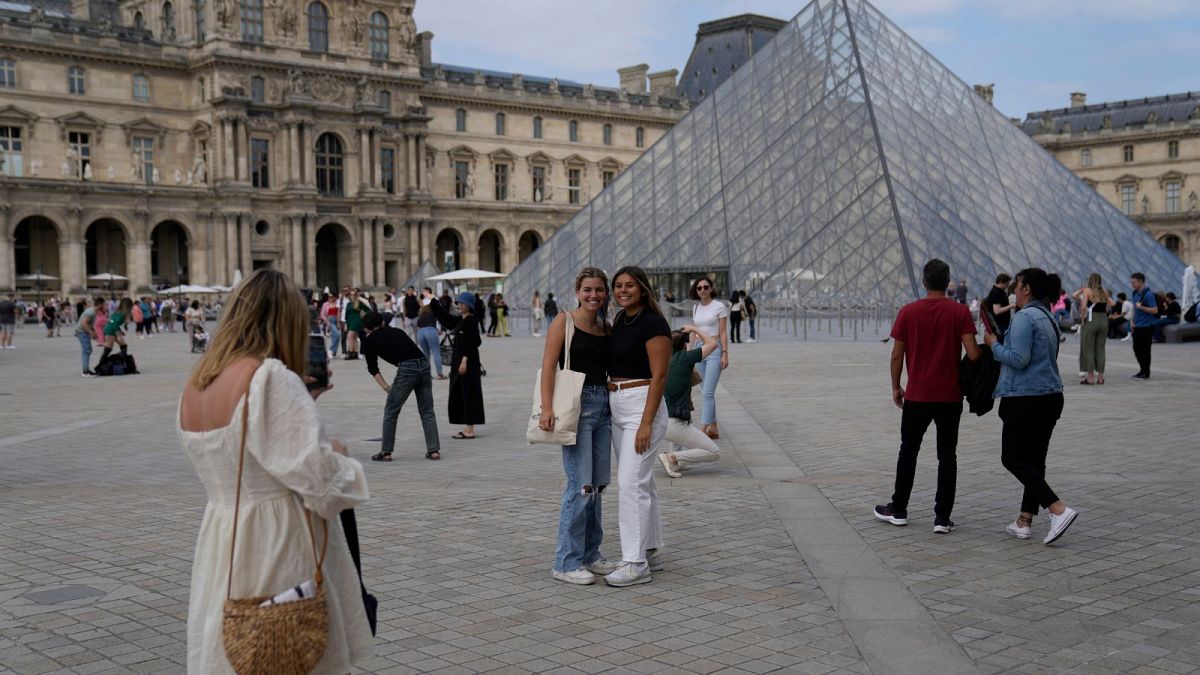 Turisti scattano foto davanti alla Piramide nel cortile del Museo del Louvre a Parigi, Francia, il 20 giugno 2022\. 