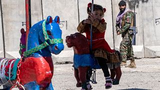 دختری در حال بازی در کابل در حالیکه یک سرباز طالبان در گوشه تصویر دیده می‌شود. عکس به تاریخ ۲۱ آوریل ۲۰۲۳