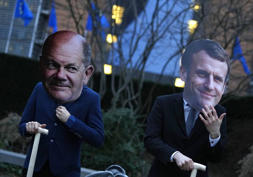 Activists wearing masks of German Chancellor Olaf Scholz and French President Emmanuel Macron hold shovels pose in front of EU headquarters in Brussels, February 2022