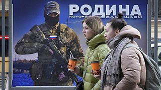 Niñas pasan frente a un puesto con la imagen de un militar ruso y las palabras "La patria que defendemos" en una exposición de fotografías militares en San Petersburgo.