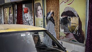 A woman walks past beauty salons with window decorations which have been defaced in Kabul, Afghanistan, Sunday, Sept. 12, 2021.