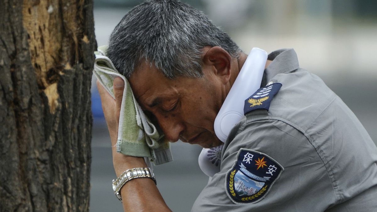 φρουρός ασφαλείας που φοράει έναν ηλεκτρικό ανεμιστήρα στο λαιμό του σκουπίζει τον ιδρώτα του στο Πεκίνο, Δευτέρα 3 Ιουλίου 2023.