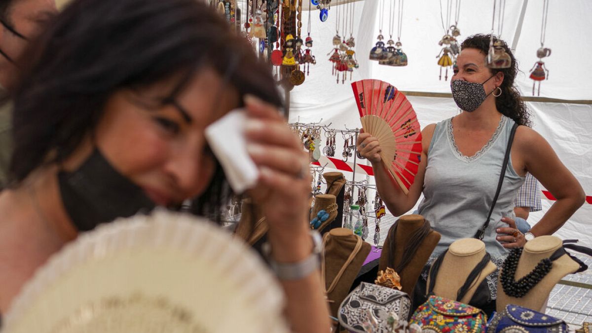 mujeres se refrescan con abanicos en el mercadillo del Rastro durante una ola de calor en Madrid, España, 15 de agosto de 2021. 