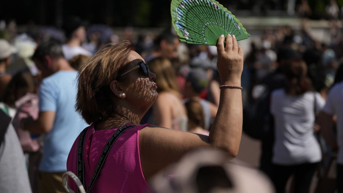 A tourist uses a fan to shade her face from the sun outside Buckingham Palace, during hot weather in London, 18 July 2022.