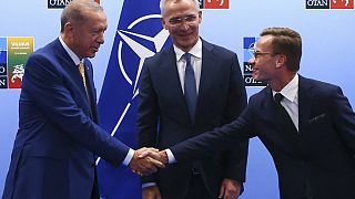 Presidente turco e primeiro-ministro sueco apertam mãos em frente ao secretário-geral da NATO