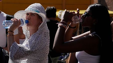 Tourists sips cold water as they shelter from a hot sunny afternoon near the Rome's Colosseum, 5 July 2023. 