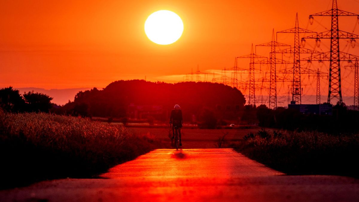 Um homem anda de bicicleta numa pequena estrada nos arredores de Frankfurt, Alemanha, enquanto o sol nasce a 9 de julho de 2023. 