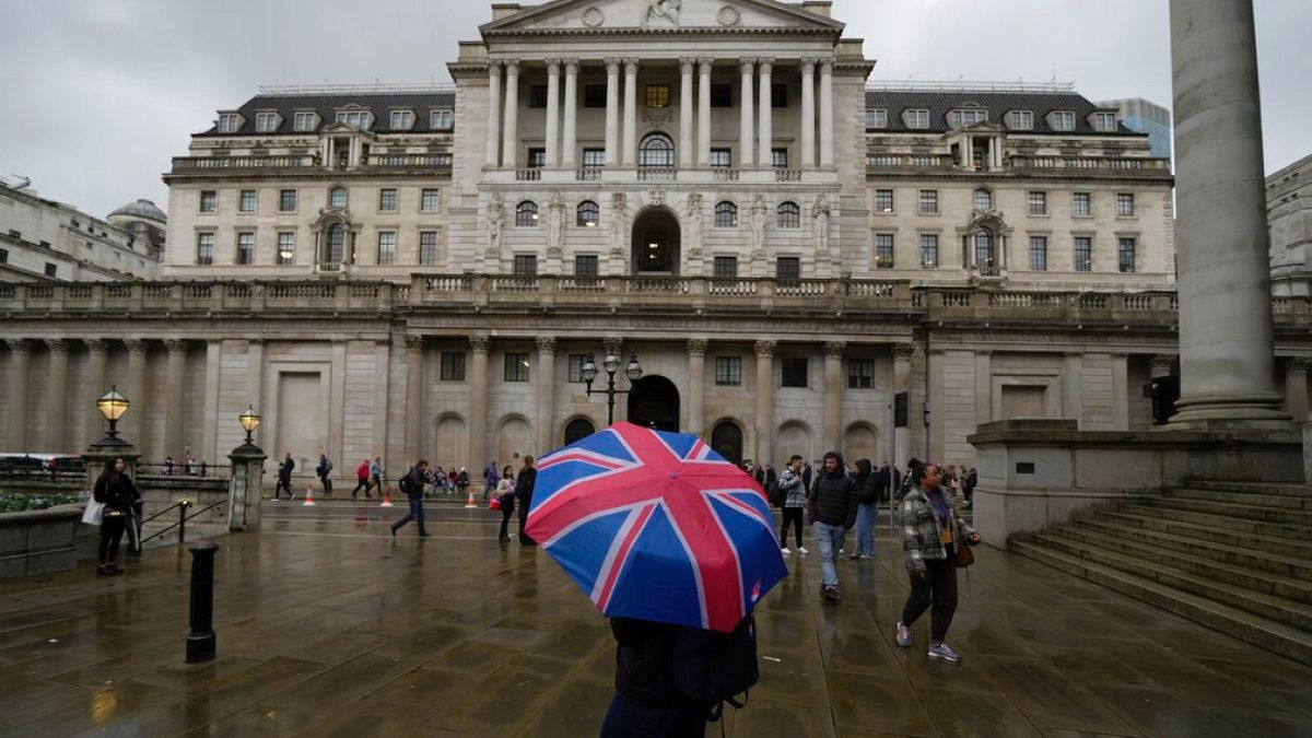 A woman with an umbrella stands in front of the Bank of England, at the financial district in London, Thursday, Nov. 3, 2022.