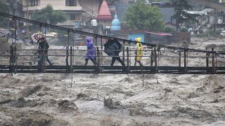 الناس يسيرون عبر جسر عبر نهر ارتفع فيه منسوب المياه بسبب الأمطار الغزيرة في منطقة كولو، هيماشال براديش، الهند. 2023/07/10