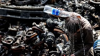عامل أجنبي يصب الماء على رأسه في ورشة للسيارات المستعملة في الشارقة.
