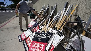 Egy férfi a sztrájkolók feliratait tartalmazó táblákkal Los Angeles-ben.
