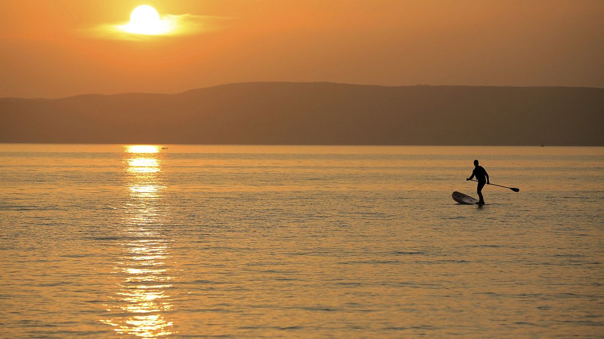 A man steers his SUP board during sunset at the Lake Balaton in Fonyod, Hungary, Tuesday, July 27, 2021