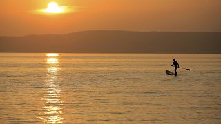 A man steers his SUP board during sunset at the Lake Balaton in Fonyod, Hungary, Tuesday, July 27, 2021