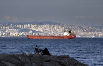 Une famille assise sur un rocher devant un cargo ancré dans la mer de Marmara attend d'avoir accès pour traverser le détroit du Bosphore à Istanbul, en Turquie, le 13 juillet