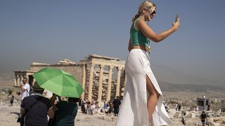 سائحة أمام قلعة الأكروبوليس في أثينا حيث سجلت درجات الحرارة ارتفاعات قياسية ما دفع بالسلطات إلى إغلاق المسرح الشهير