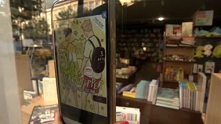 A szóban forgó könyv borítója egy okostelefon kijelzőjén, a Líra egyik budapesti üzletének kirakata előtt - 2023. 07. 15-én