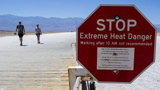 يافطة تحذر من درجات حرارة مرتفعة بشكل قياسي في وادي الموت وسائحان يتجولان في المكان