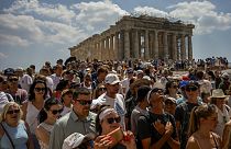 Atop the Acropolis ancient hill, tourists visit the Parthenon temple, background, in Athens, Greece