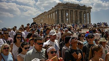 Atop the Acropolis ancient hill, tourists visit the Parthenon temple, background, in Athens, Greece