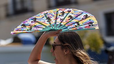 A woman protects herself with a hand-held fan from the sun in Madrid, Spain, Monday, July 10, 2023. 