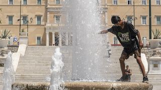 Athéni férfi a görög parlament épülete előtt hűti magát egy szökőkútban