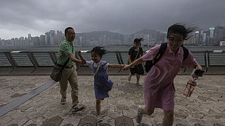 سياح يركضون من البر الرئيسي الصيني على طول كورنيش خلال إعصار في هونغ كونغ، 17 يوليو 2023.