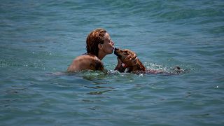 A tengerben hűsöl egy nő a kutyájával Barcelonában 2023. július 17-én