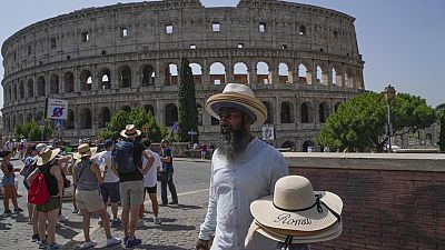 A street vendor walks with hats in front of the Colosseum in Rome