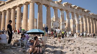 Tourist sit in front of the five century BC Parthenon temple at the Acropolis hill during a heatwave, Thursday 13 July 2023.