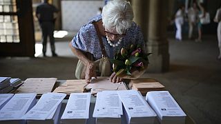 A woman holding a bouquet of flowers tries to select her ballots to vote at a polling station in Barcelona, Spain, Sunday July 23, 2023.