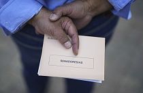 Ein Mann wartet vor einem Wahllokal in Madrid mit einem Wahlzettel in seiner Hand