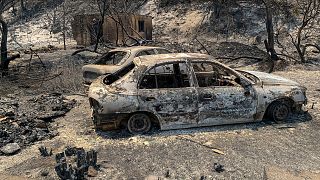 بقایای سوخته خودروها در جاده‌ای پس از آتش سوزی جنگل‌ها در یونان