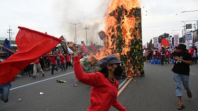 Protesters run past a giant military boot after setting it up on fire as they march towards Congress for a demonstration in Quezon City, suburban Manila on July 24, 2023