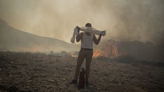 Un hombre se proteje de los gases del fuego con una toalla mojada mientras ayuda en las tareas de extinción en Rodas, Grecia.