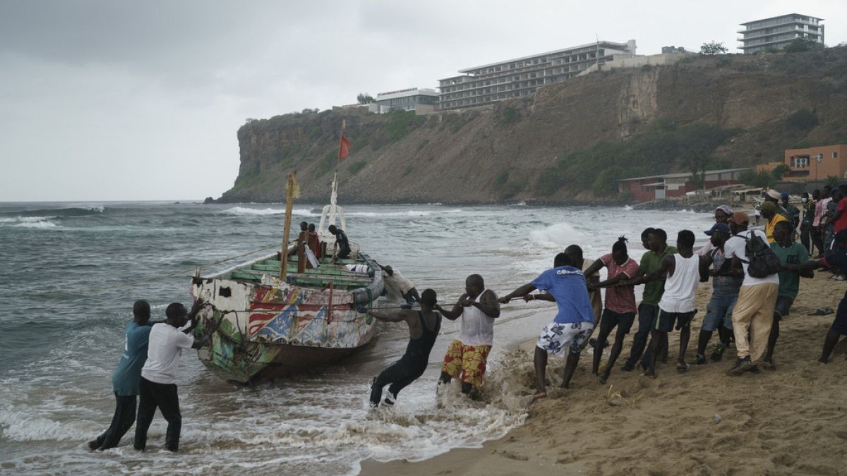 Las personas trabajan juntas para sacar, según los lugareños, el bote volcado a tierra en la playa donde varias personas fueron encontradas muertas en Dakar, Senegal, el lunes