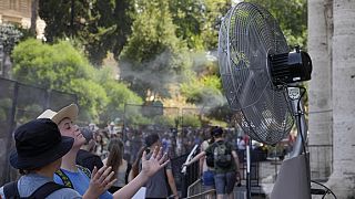 Touristen kühlen sich in der Nähe eines Ventilators ab, während sie in der Schlange vor dem Kolosseum in Rom stehen, 18. Juli 2023.